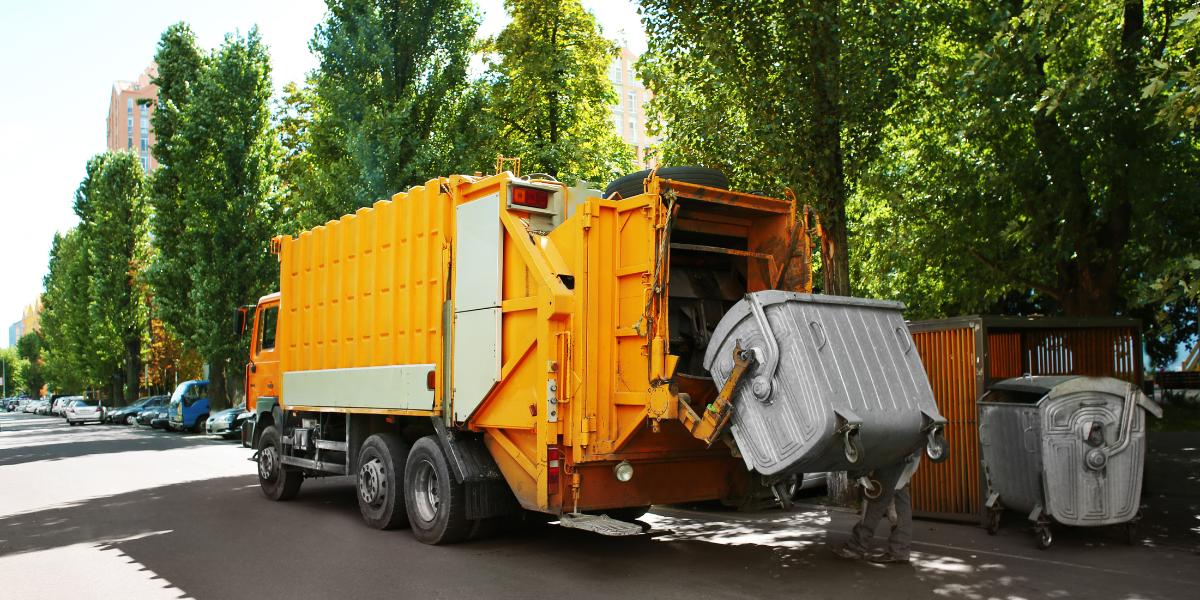 yellow garbage truck lifting up a large garbage bin to effectively manage loss prevention for waste management